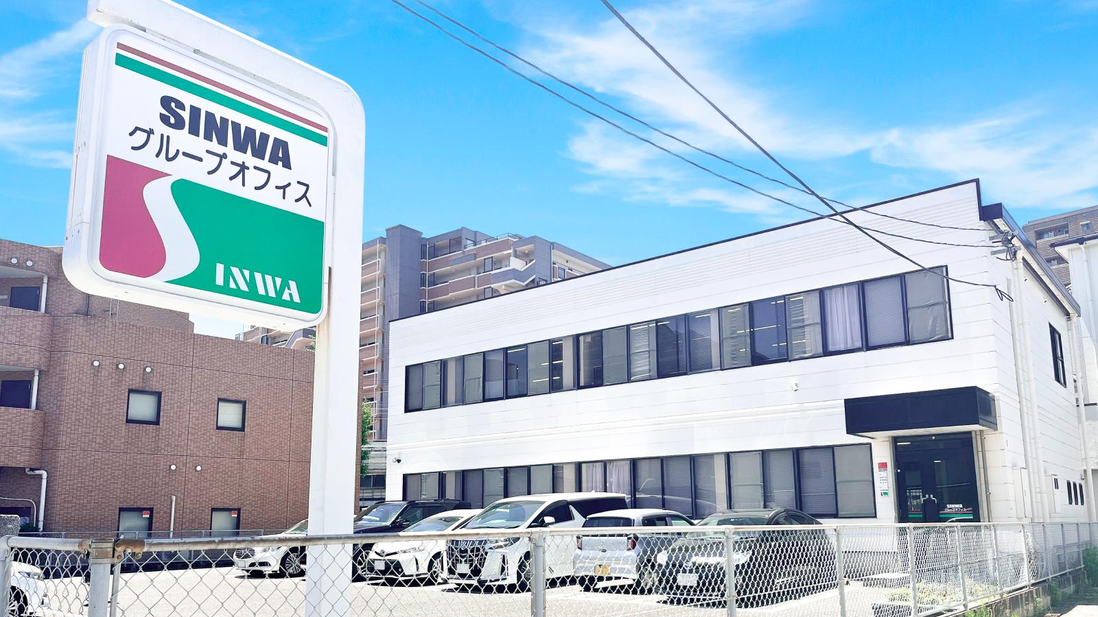 青空の下に立つ「SINWA グループオフィス」の看板と、駐車場に面したオフィスビルの外観。